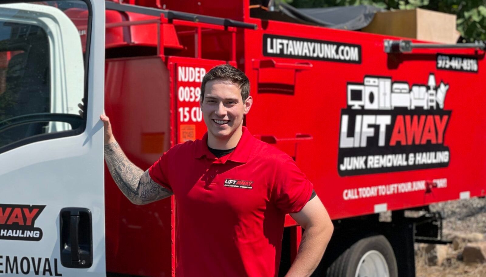 Man in red shirt stands next to a red Lift Away junk removal truck, smiling.