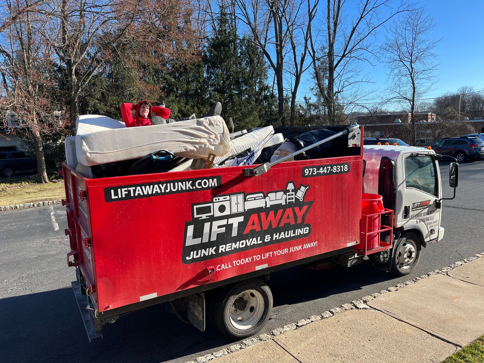 Red Lift Away junk removal truck filled with discarded items parked on a street.