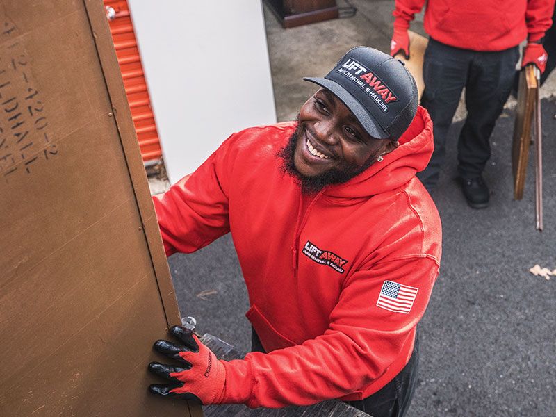 Man in red hoodie and hat from Lift Away smiles while carrying furniture. Another person is visible.
