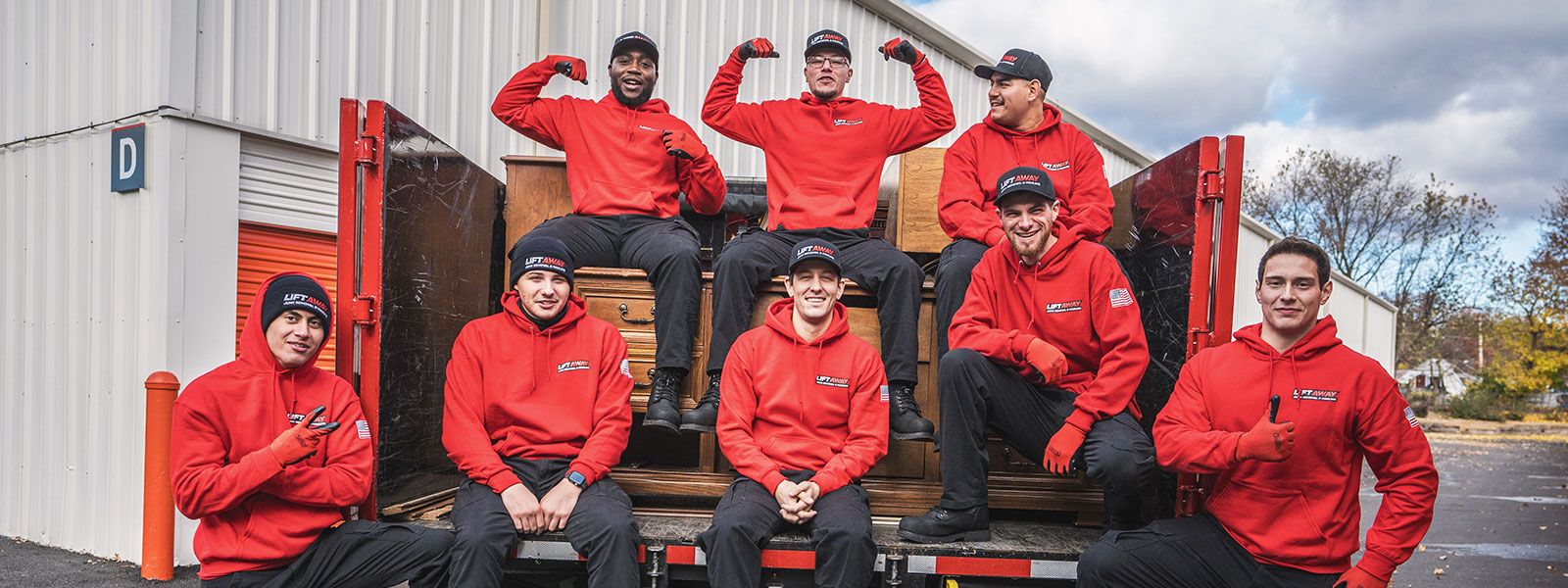 Group of movers in red hoodies posing on the back of a truck.