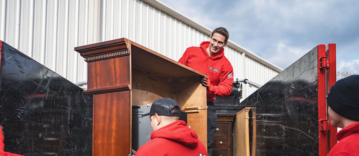 Movers in red loading furniture into a truck outside a warehouse.