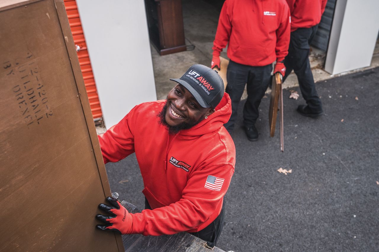 Movers in red hoodies carrying furniture out of a storage unit. The lead mover is smiling.