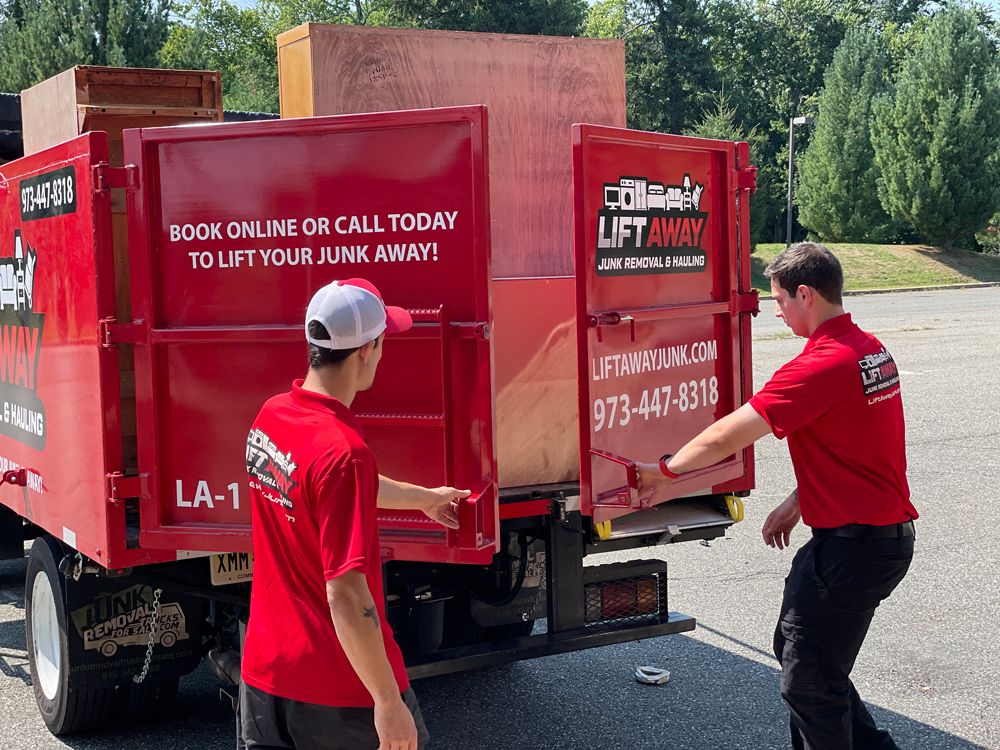 Two men in red shirts opening the back of a red junk removal truck in daylight. Text on the truck reads 