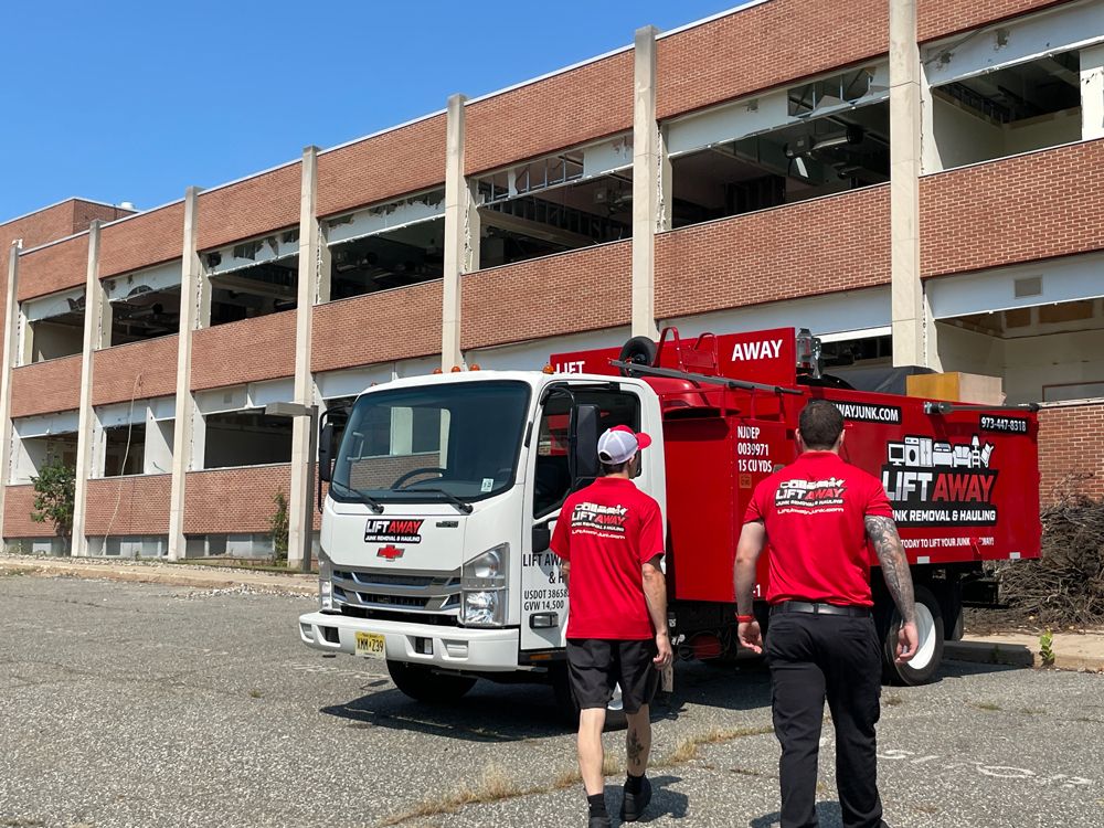 Two people in red shirts walk toward a white truck with a red aerial lift in front of a brick building.