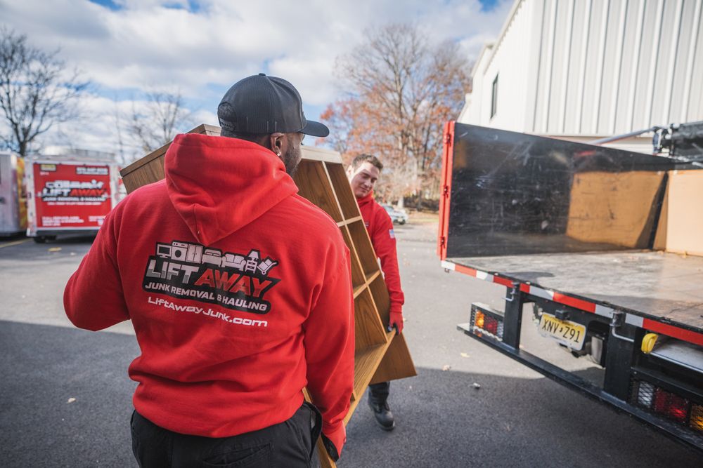 Two people in red hoodies loading a wooden shelf into a truck bed outdoors.