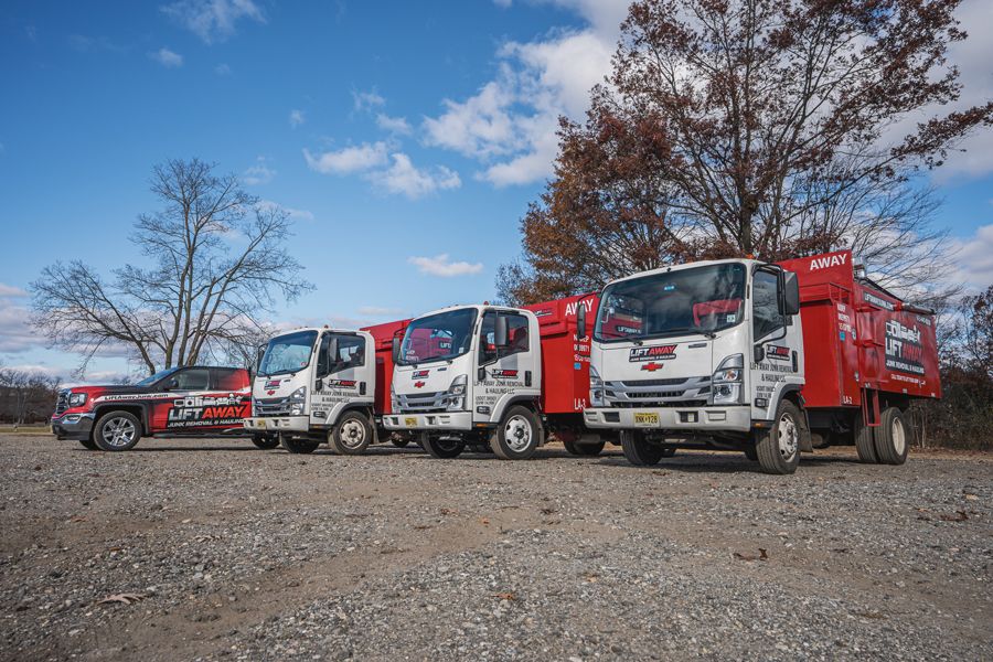 Four red and white work trucks parked outdoors on gravel, under a partly cloudy blue sky.