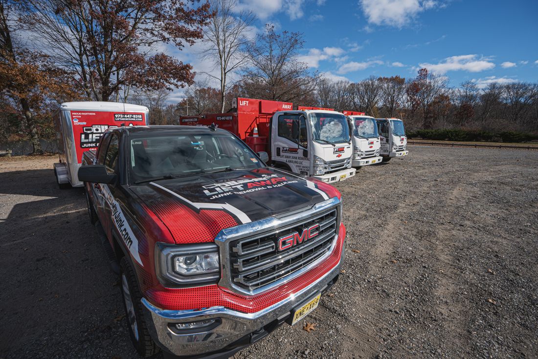 GMC truck with red and black details pulling a trailer, parked near red and white work trucks. Sunny day.