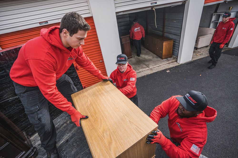 Movers in red hoodies load a wooden dresser into a storage unit.