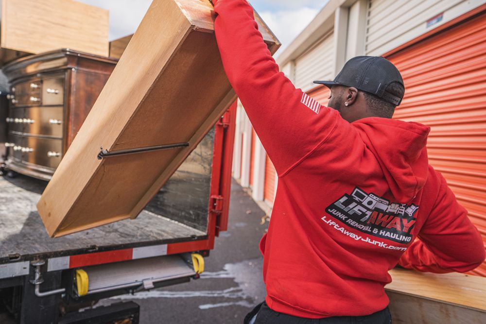 Man in red hoodie lifts furniture into a moving truck at a storage facility.