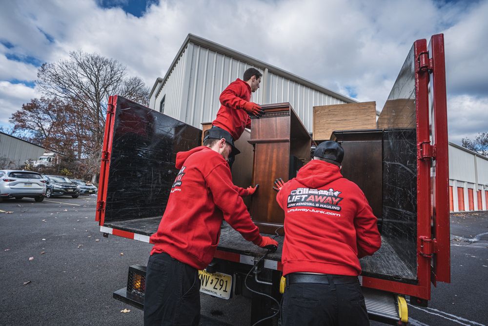 Three movers in red hoodies loading furniture into a red dump truck in front of a storage facility.