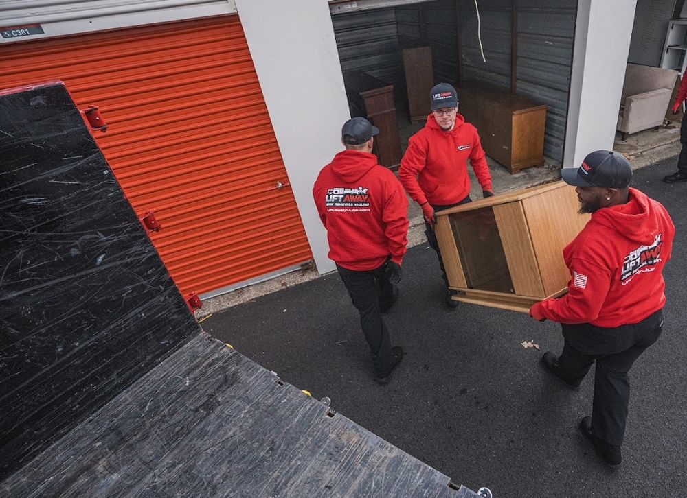 Movers in red jackets carrying a wooden cabinet towards an orange storage unit.