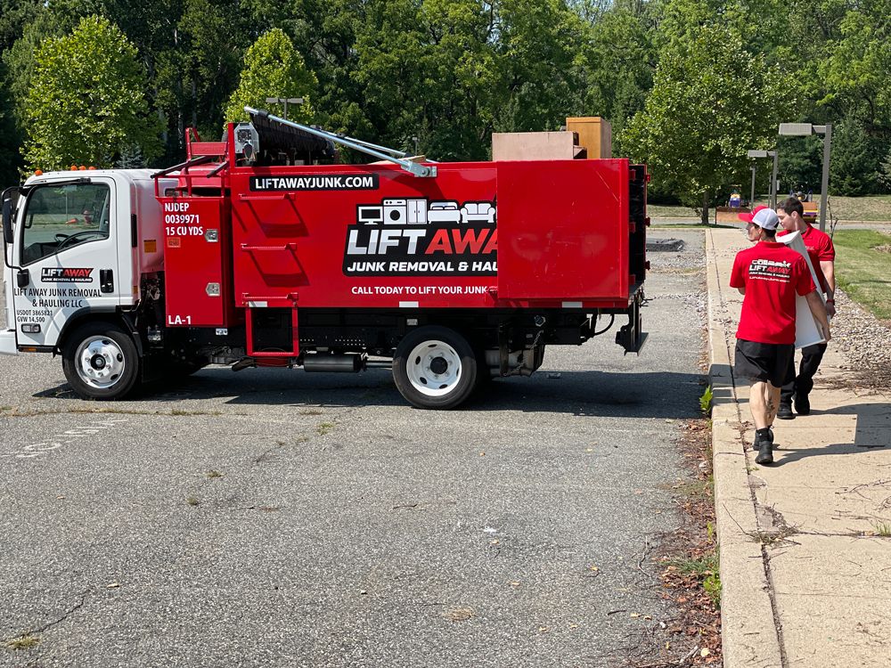 Red Lift Away junk removal truck parked, two people in red shirts walking away.