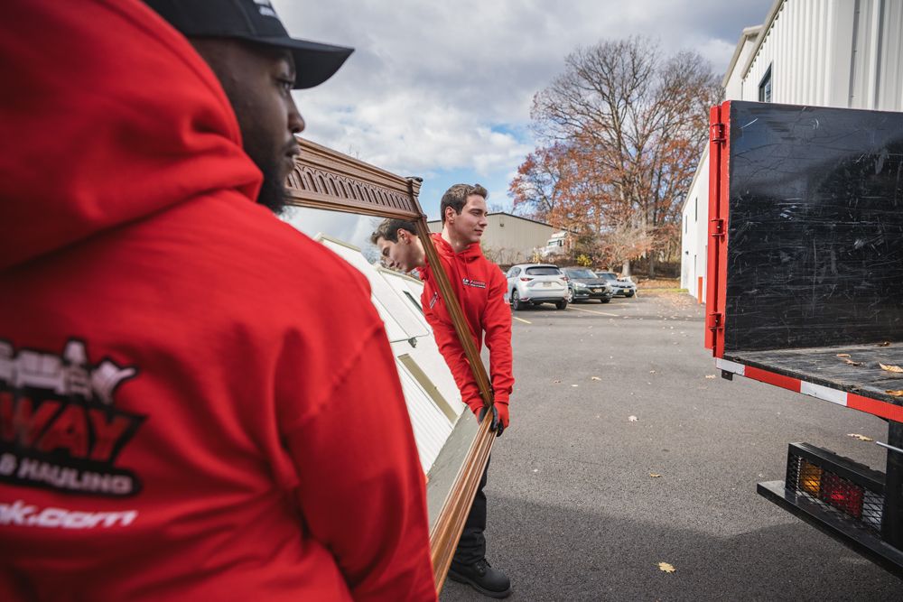 Three men in red hoodies loading furniture into a truck on a cloudy day.