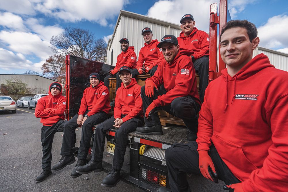 Group of nine people in red hoodies and hats sit on a truck bed outdoors.