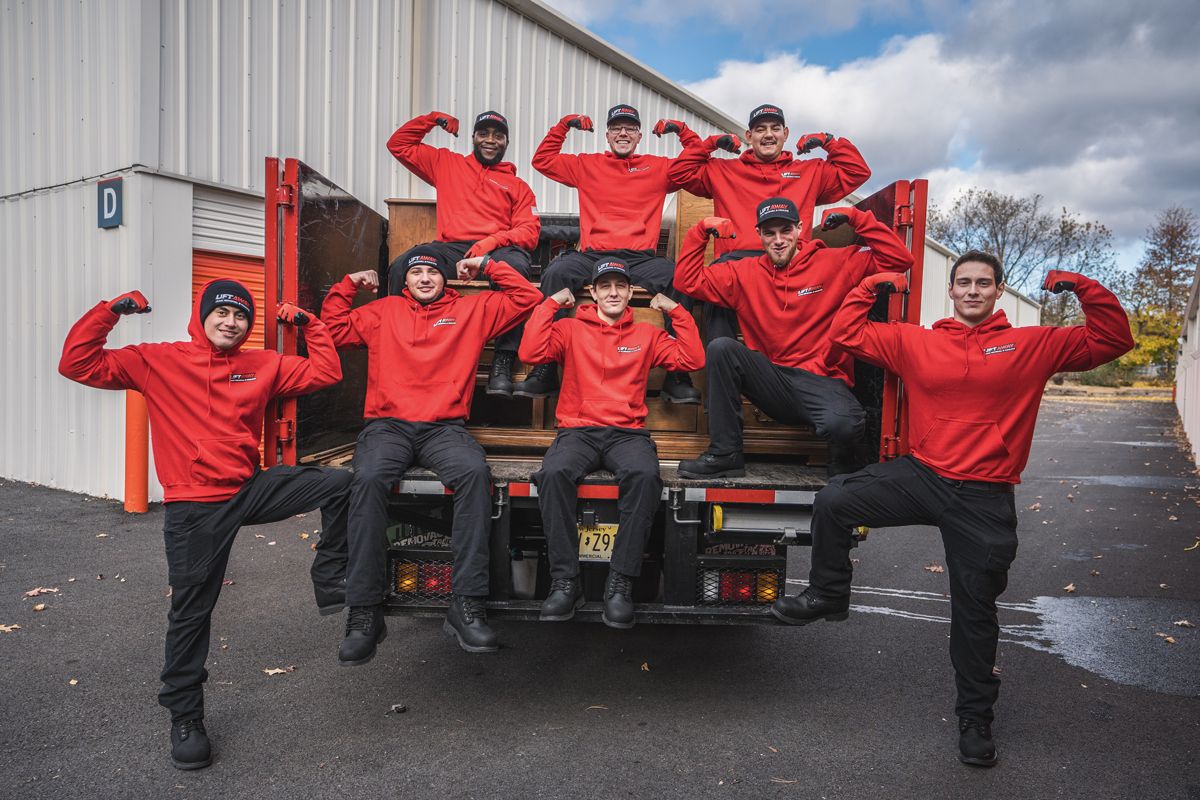 A team of people in red and black uniforms posing with trucks in a gravel lot under a blue sky.