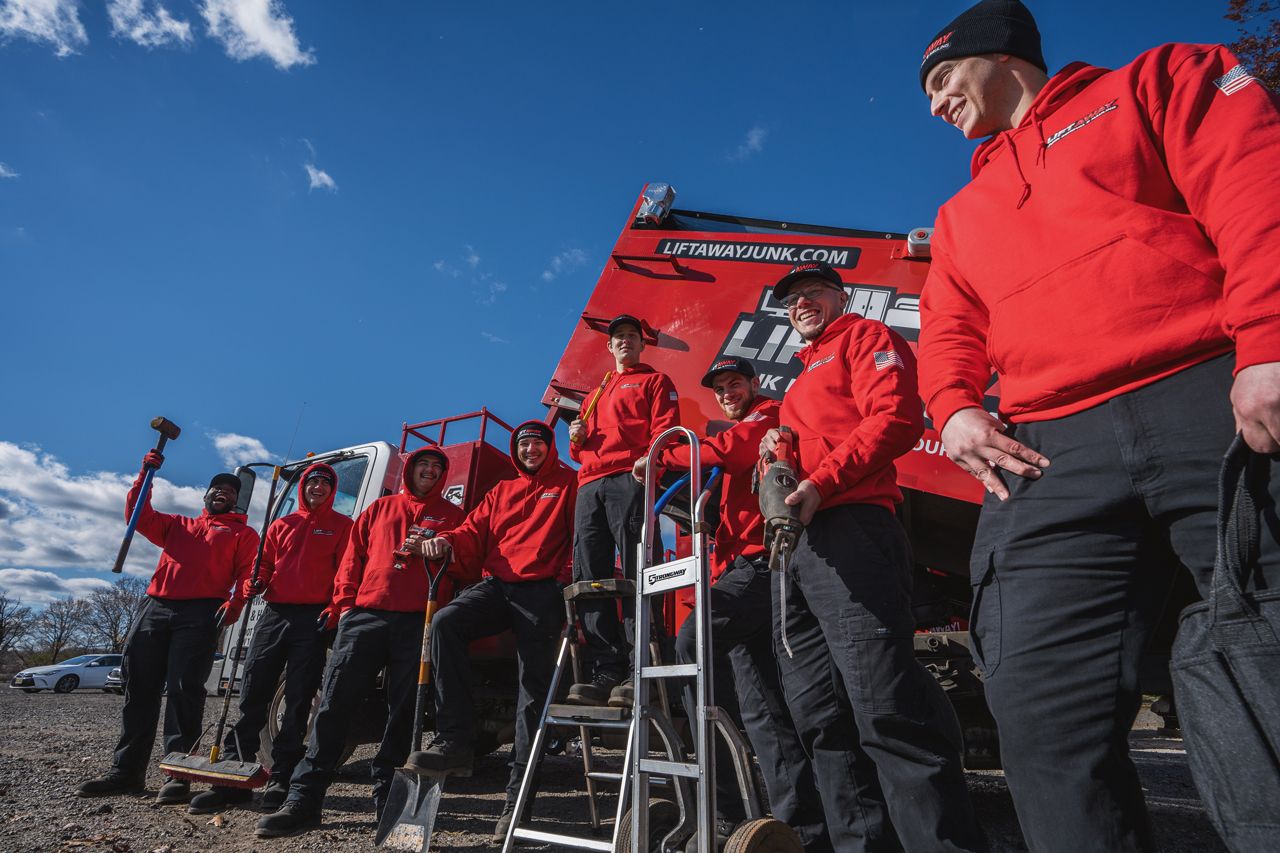 A man in a red hoodie stands arms crossed in front of a row of trucks and crew in red uniforms.