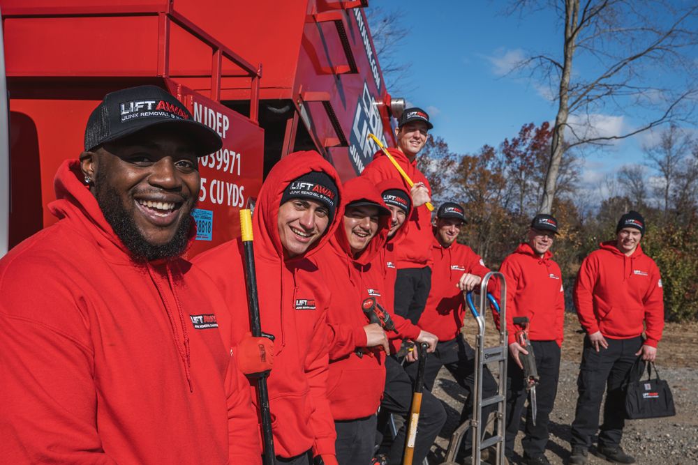 Group of movers in red hoodies smiles, standing near a red truck outdoors.