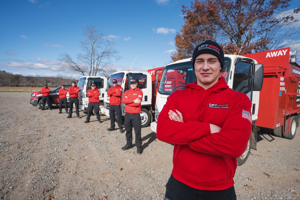 A man in a red hoodie with arms crossed stands in front of a line of red trucks and a crew in matching uniforms.
