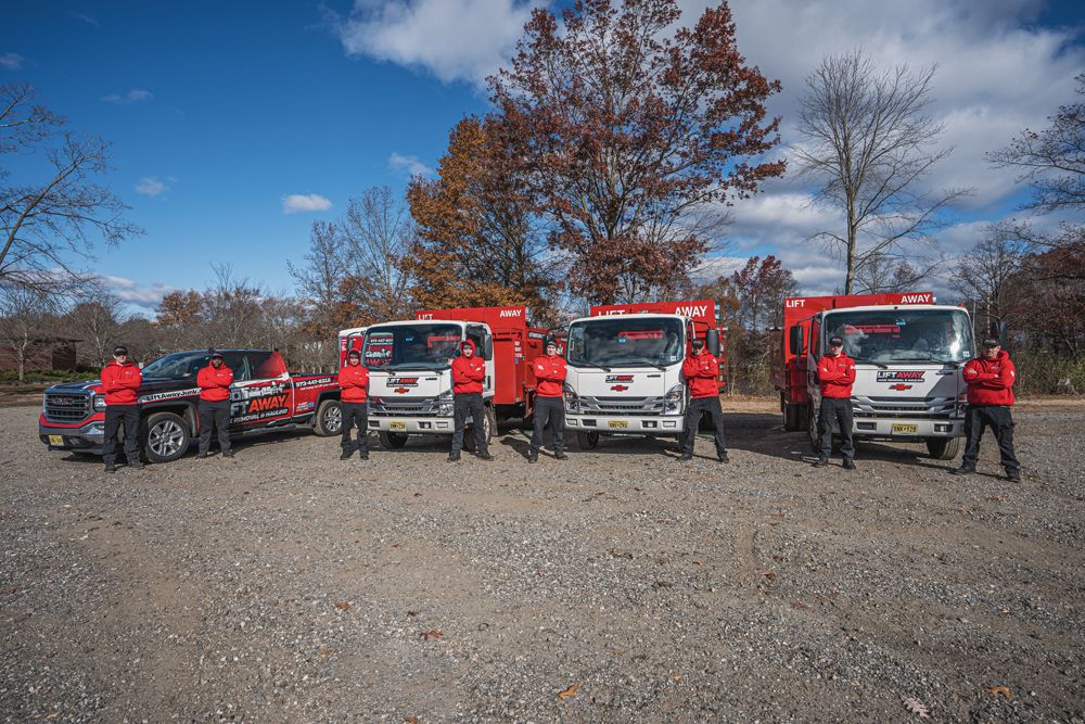 A team of people in red and black uniforms posing with trucks in a gravel lot under a blue sky.