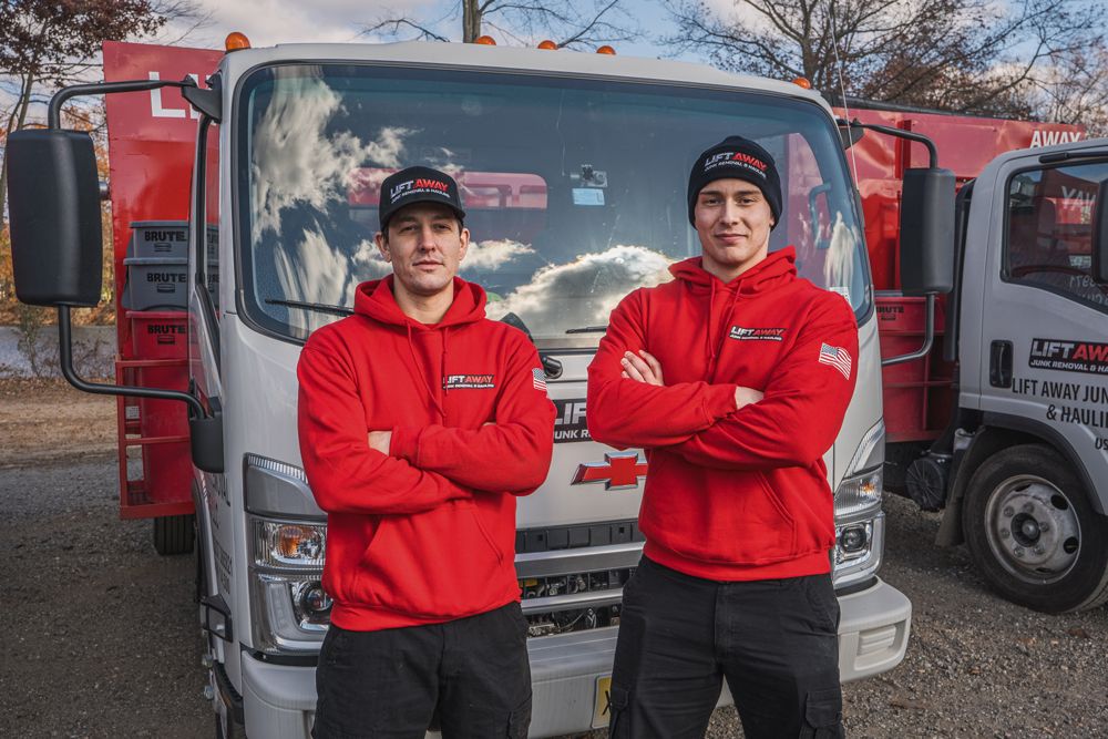 Two men in red hoodies stand in front of a truck, arms crossed, smiling.