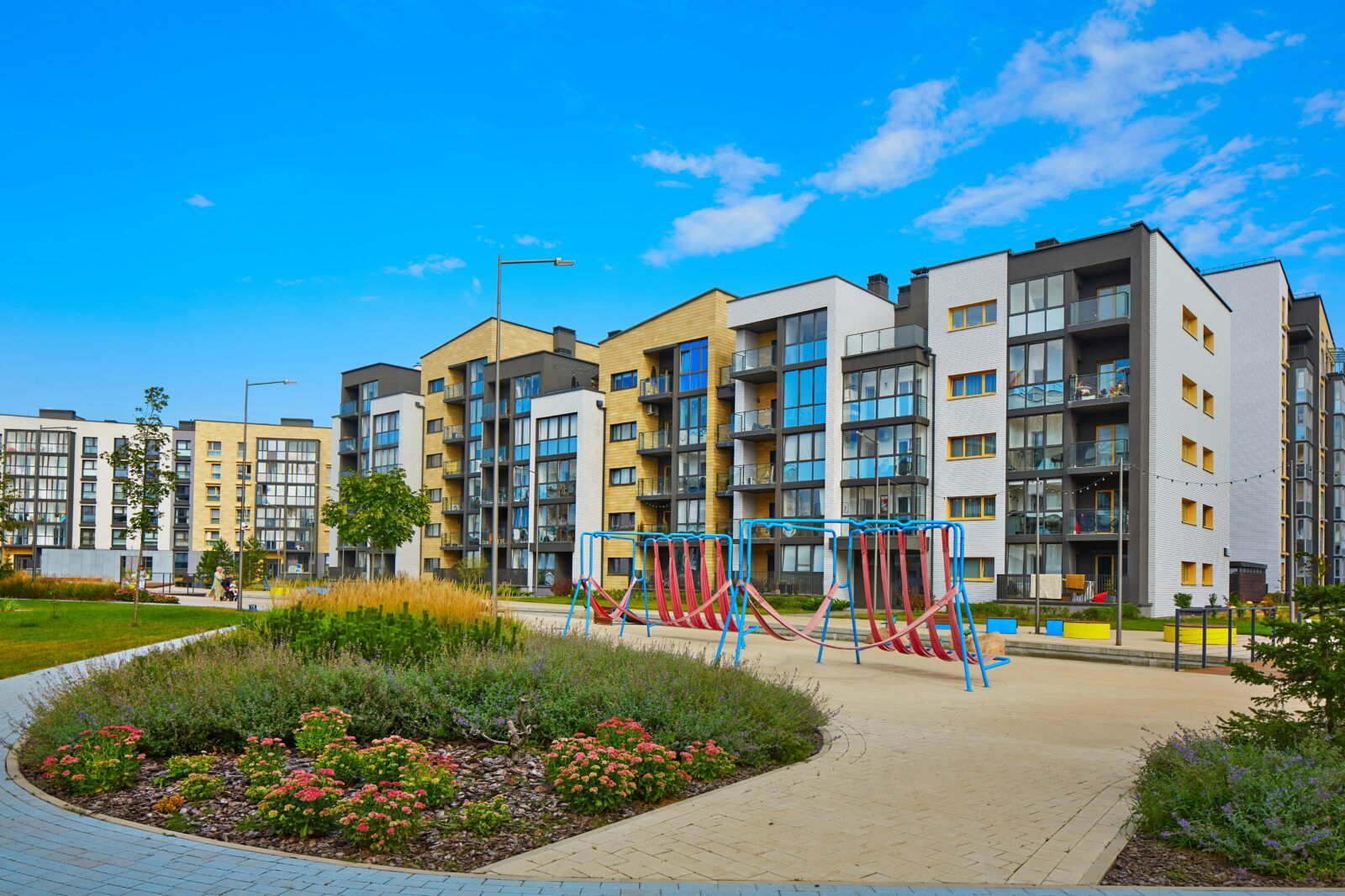 Apartment complex with a playground on a sunny day. Buildings are various colors; blue sky.