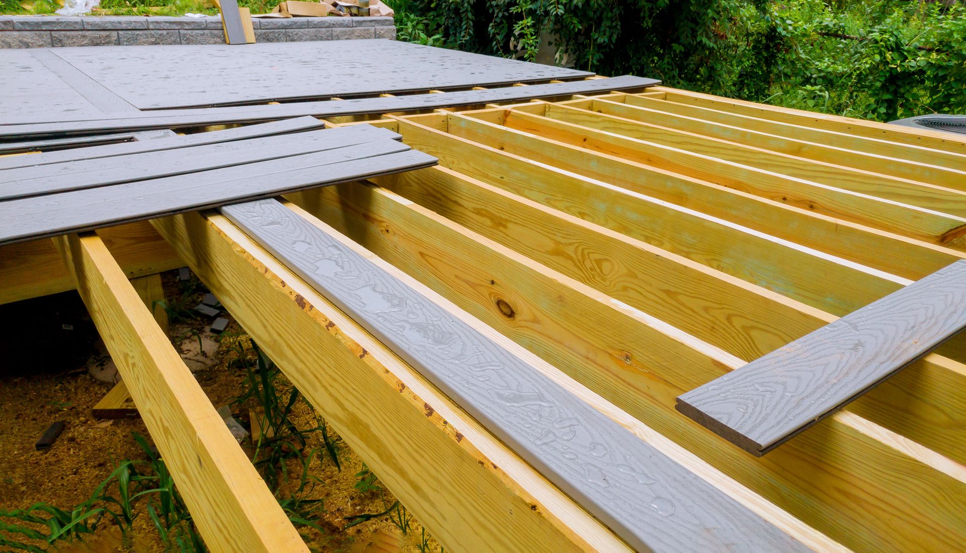 Deck under construction, light-colored wood framing, gray composite decking boards partially installed.
