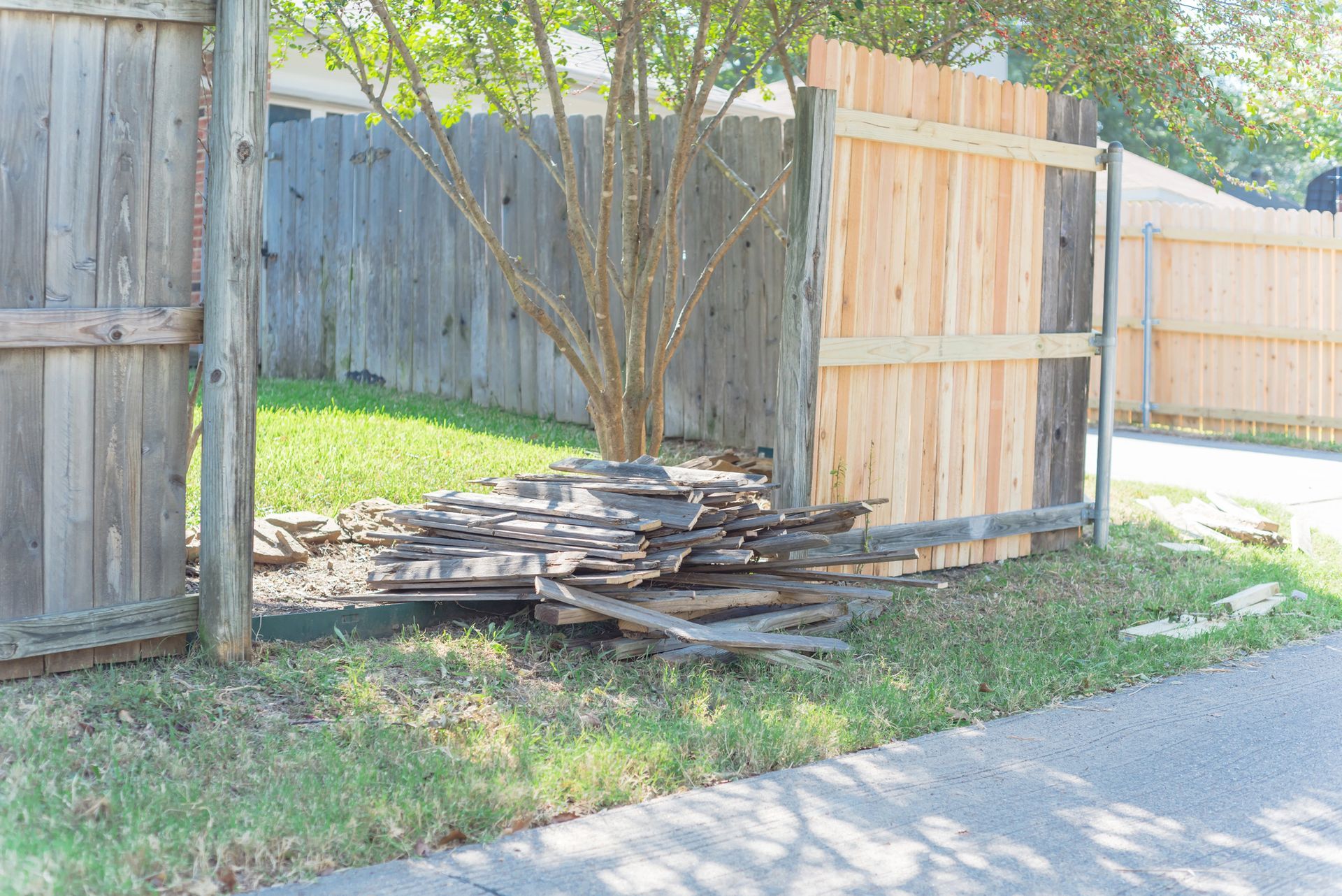 Pile of old fence planks in front of a newly built wooden fence with green grass.