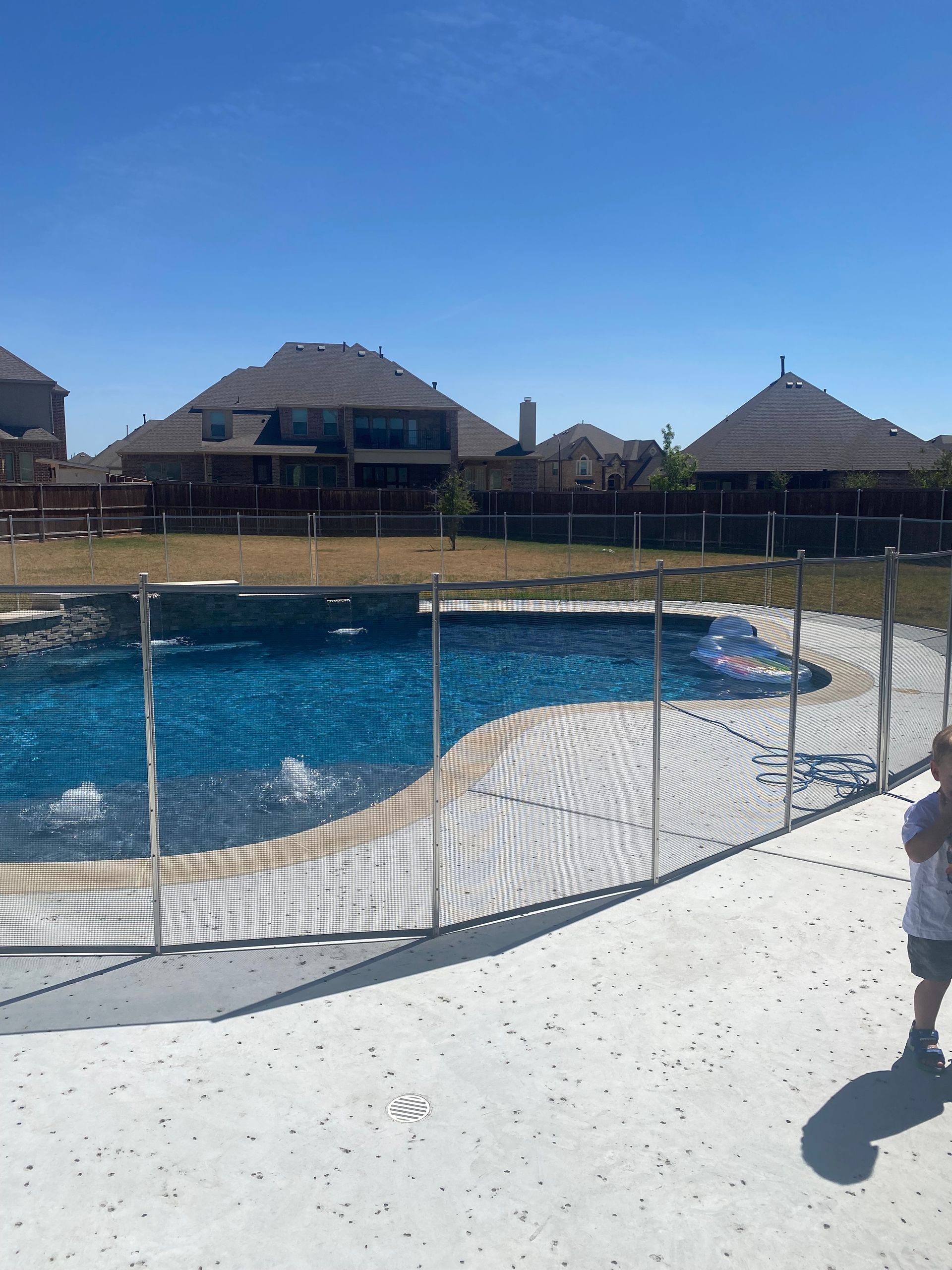 Pool with a net fence and thatched-roof buildings under a clear blue sky.