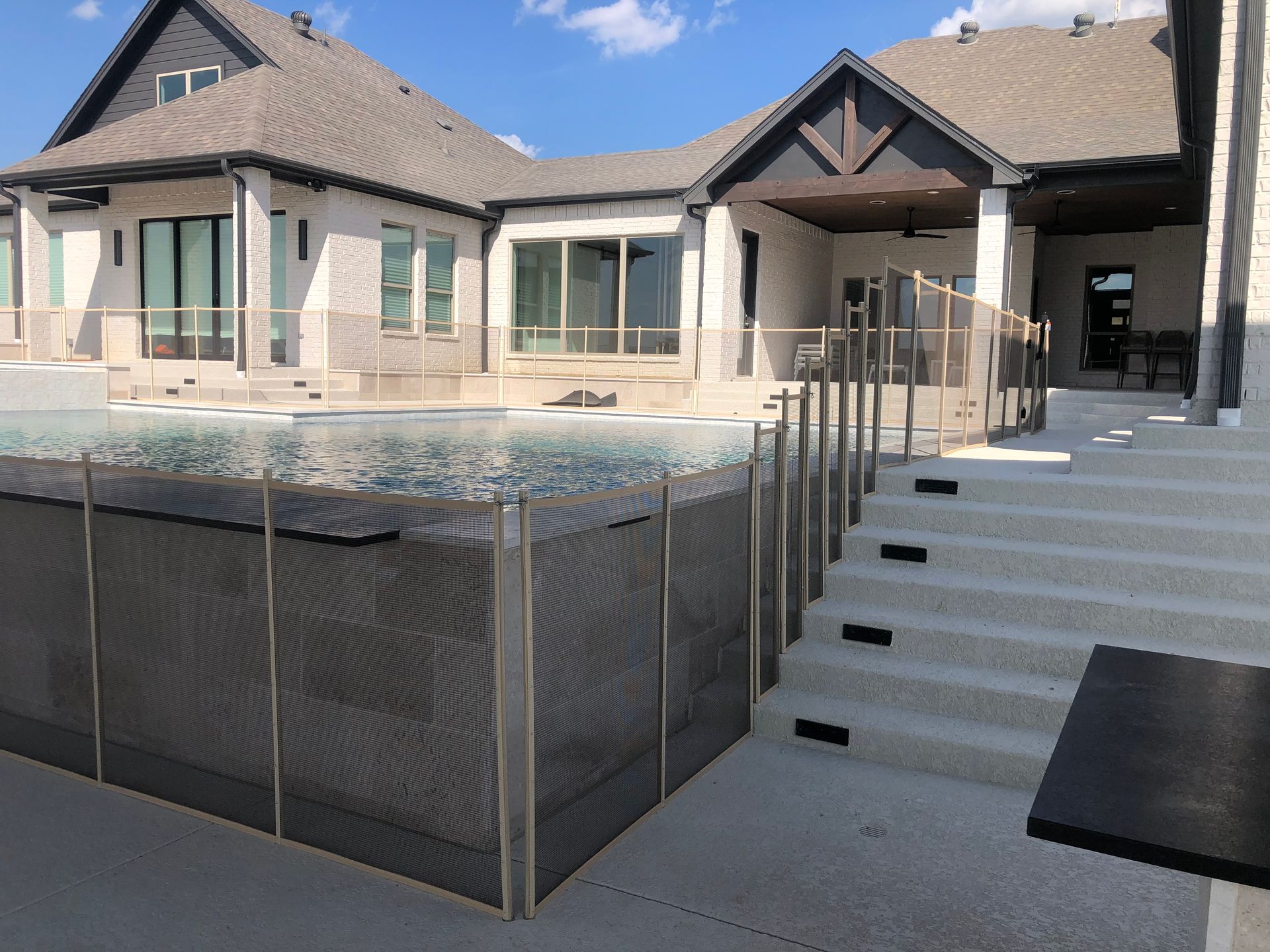Backyard patio with swimming pool, stone steps, and a modern house under a bright sky