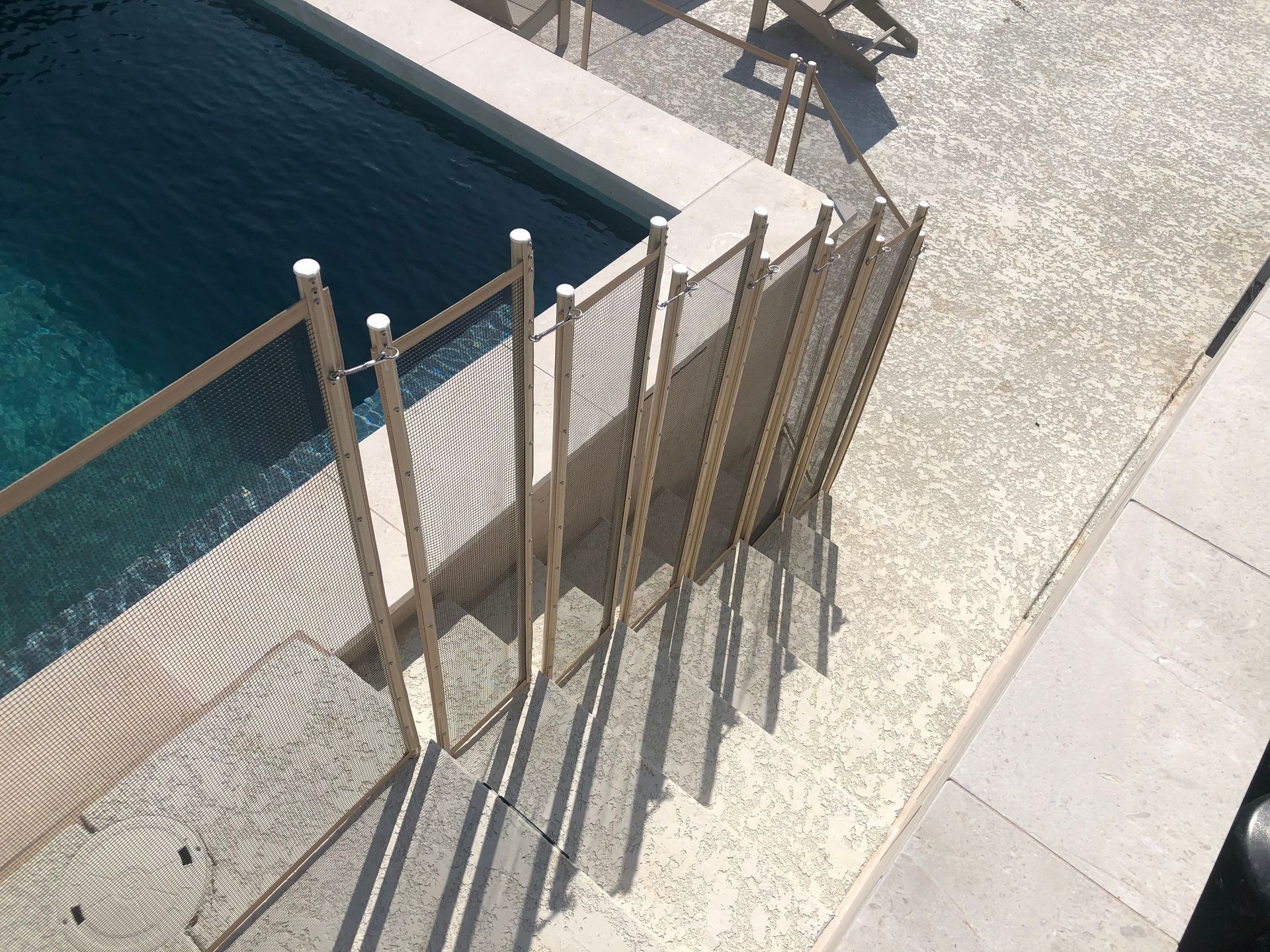 Poolside metal railing casting long shadows on a sunlit stone deck beside dark blue water