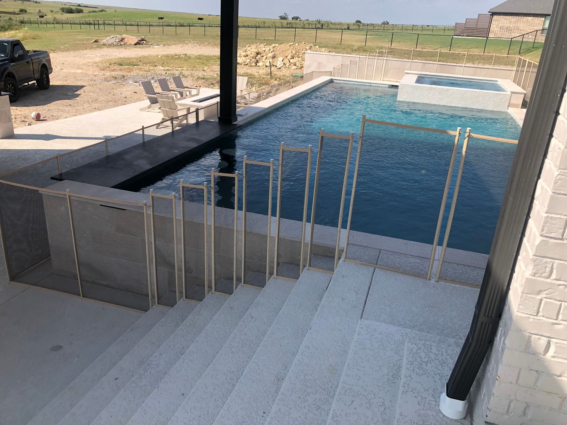 Backyard swimming pool with white steps and glass railing, viewed from a covered patio.