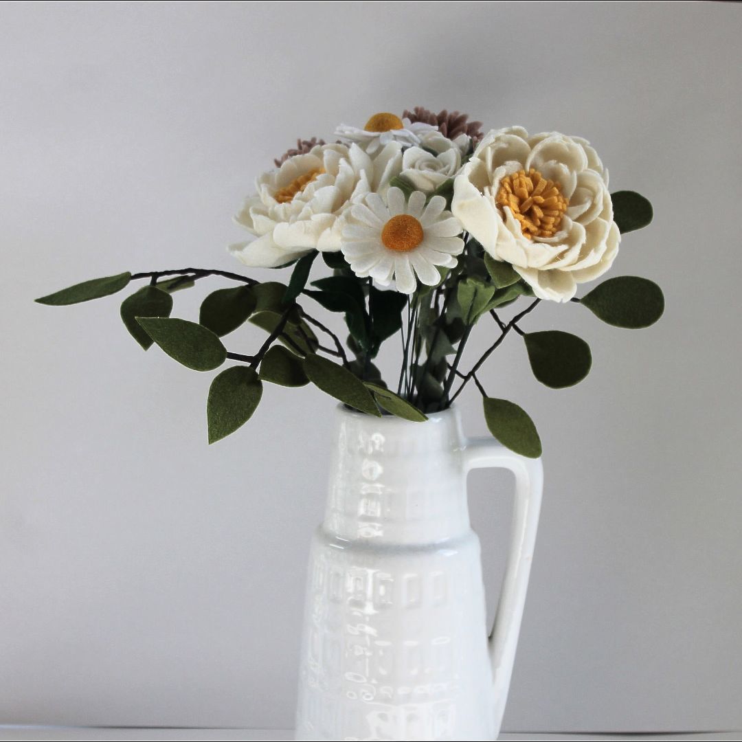 Boeket witte vilten bloemen in een witte keramische vaas.