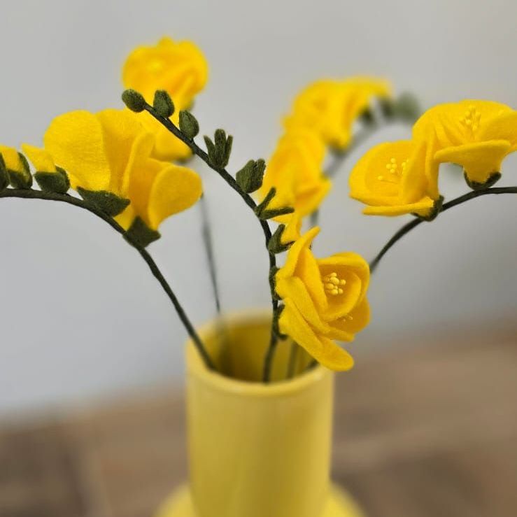 Gele vilten fresia's in een gele vaas op een houten tafel.