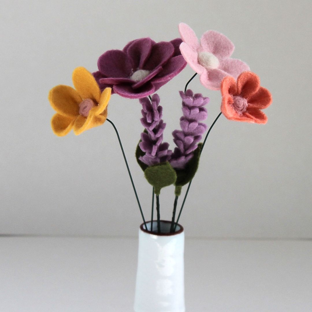 Vilten bloemenboeket in een witte vaas: goudkleurige, paarse, roze en oranje bloemen met groene stelen.