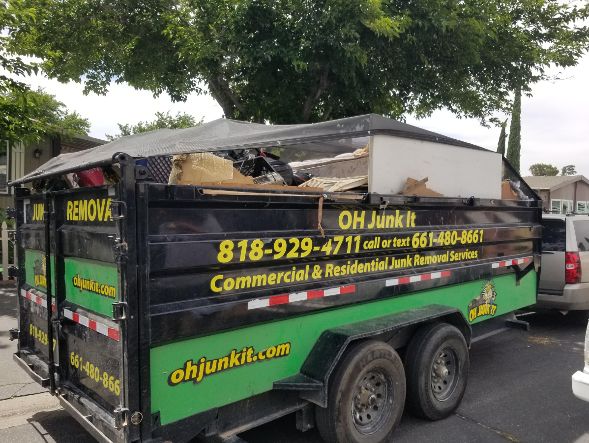 Black and green OH Junk It trailer, filled with debris, parked on a street. 818-929-4711.