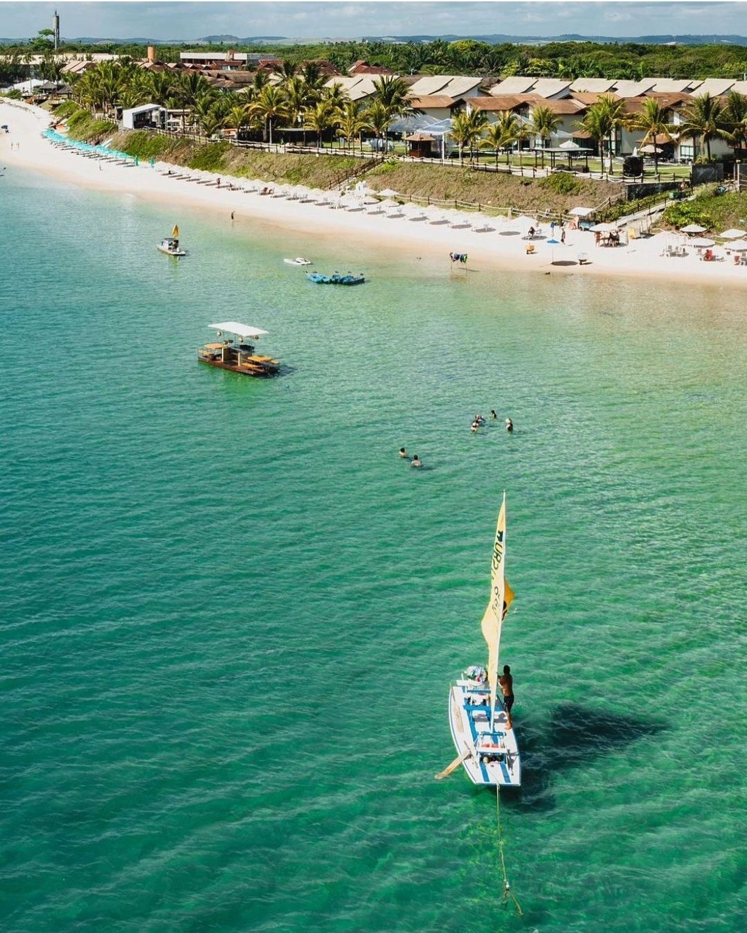 Uma vista aérea de um veleiro no oceano perto de uma praia.