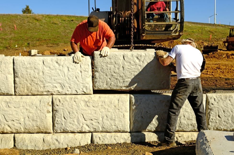 Two Men Are Working on a Stone Wall With a Bulldozer in the Background — Ape Earthmoving In Highfields, QLD