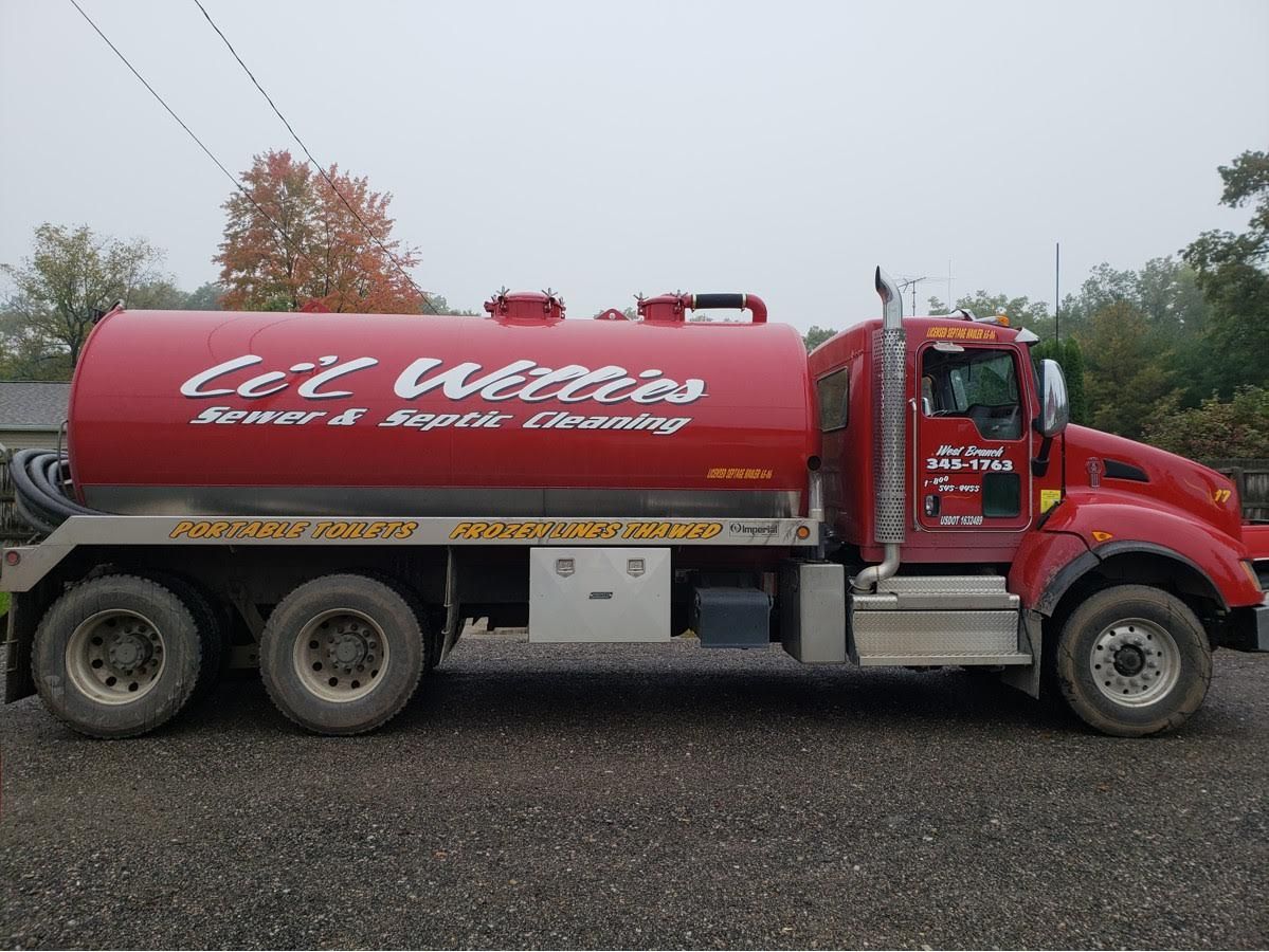 A red septic tank truck is parked in a gravel lot