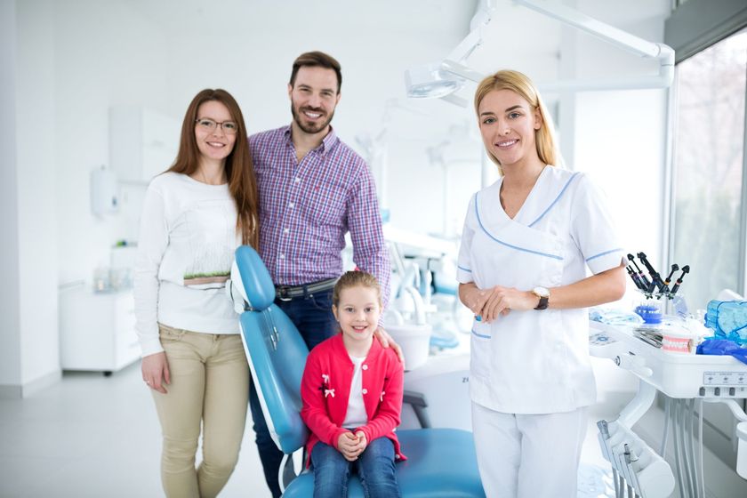 Dental clinic staff with a smiling family in a bright exam room, including a child in a blue dental chair Dental clinic staff with a smiling family in a bright exam room, including a child in a blue dental chair