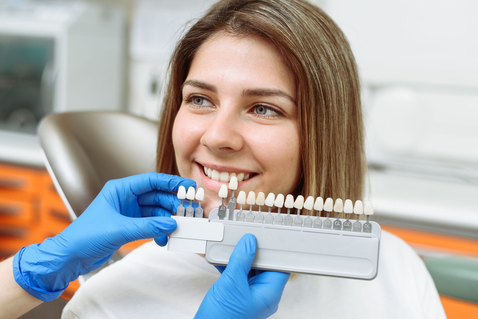 Dentist holding tooth shade guide near smiling patient in a clinic Dentist holding tooth shade guide near smiling patient in a clinic
