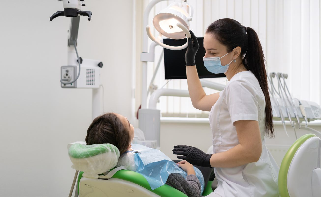 Dentist examining a patient in a dental chair while wearing a mask in a bright clinic room Dentist examining a patient in a dental chair while wearing a mask in a bright clinic room