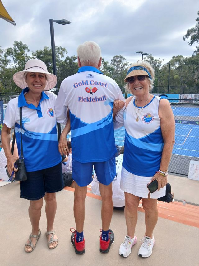 Three Gold Coast Pickleball Members are standing next to each other on a pickleball court wearing club  merchandise. 