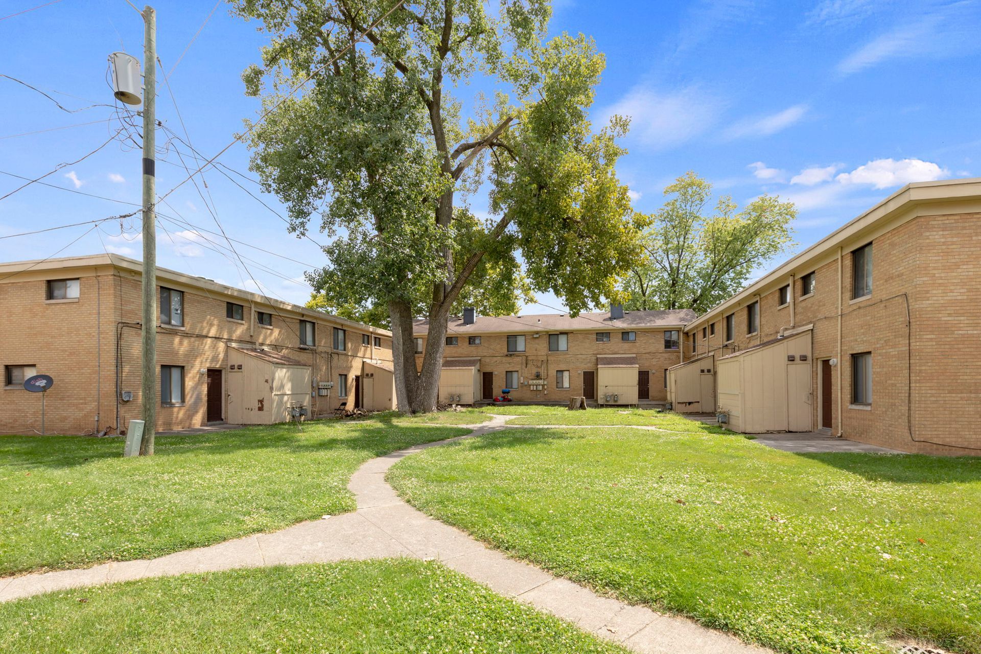 Apartment complex with brick buildings, a central grassy courtyard, and a large tree.