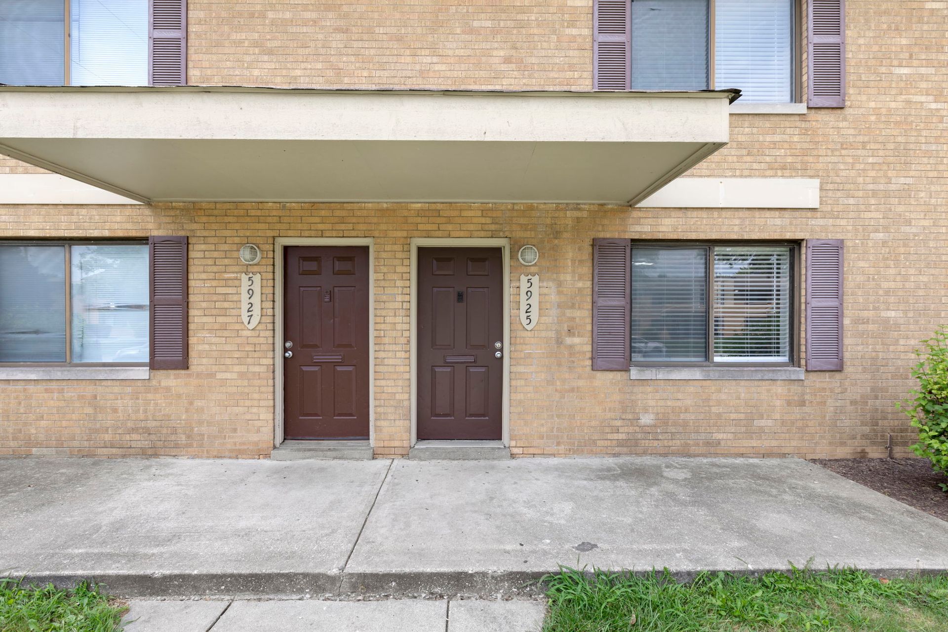 Two brown doors with numbers on a brick building. A small covered porch extends above.