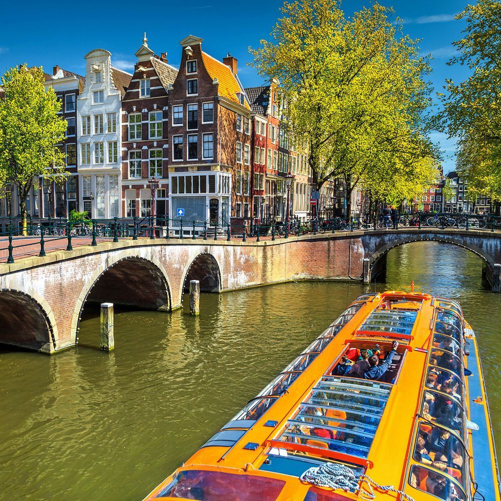 Amsterdam's  canal houses with a boat on the canal next to a bridge with trees
