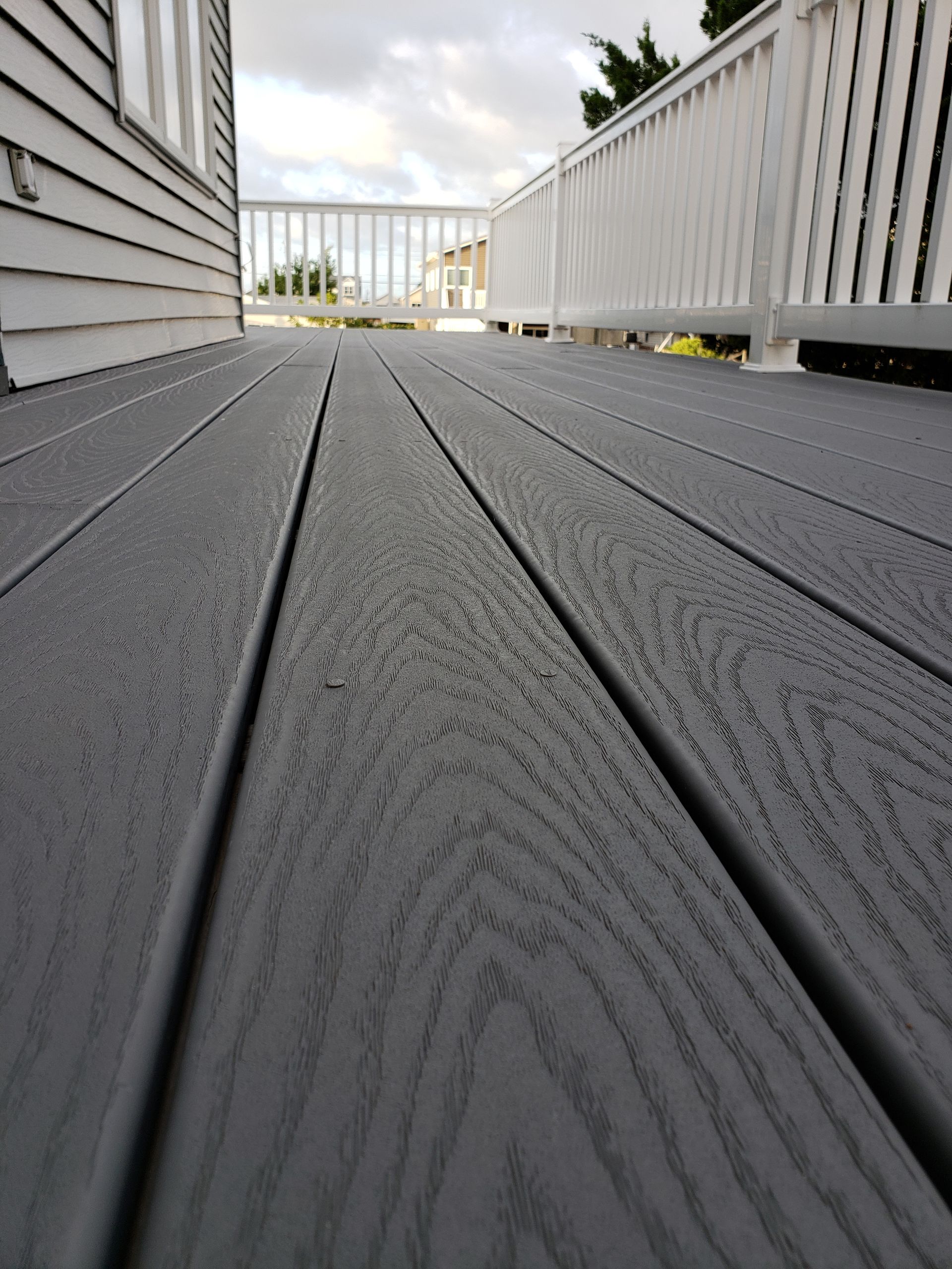 Low-angle view of a dark gray wooden deck leading to a white railing and house siding