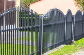 Black metal fence with arched gate beside a house and grassy yard