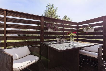 Outdoor patio seating with wicker chairs and a glass table beside a dark wooden privacy fence