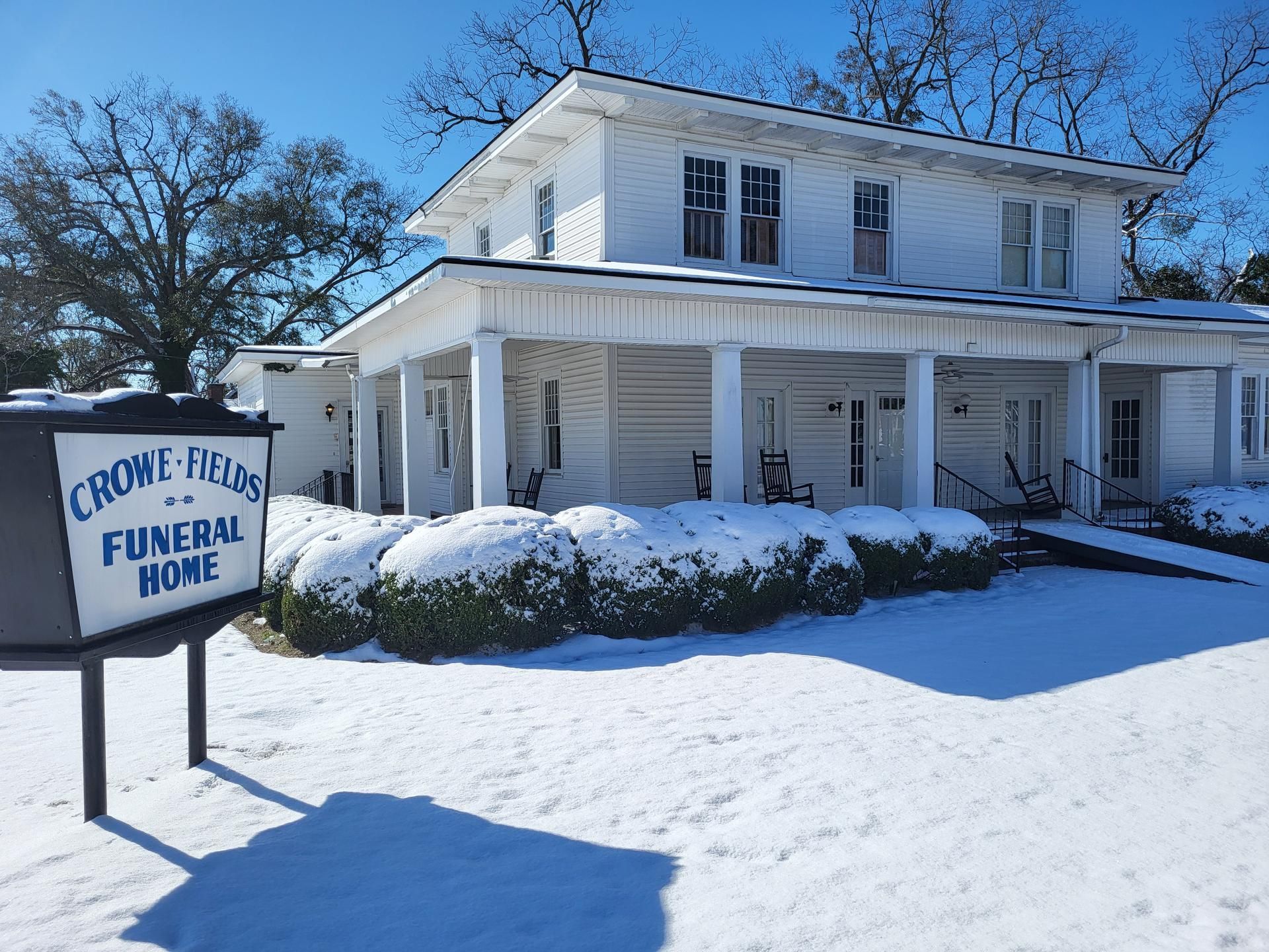 Snow-covered white funeral home with sign reading “Crouse & Sons Funeral Home”