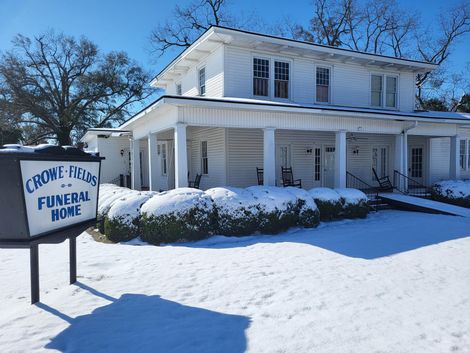 Snow-covered white funeral home with sign reading “Crouse & Sons Funeral Home”